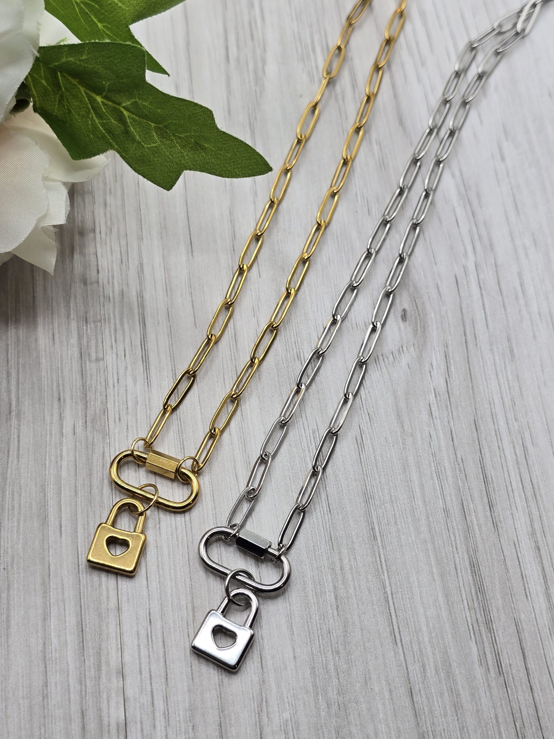 Picture shows two paperclip chain necklaces with carabiner clasp and lock charm with heart in the center.  Partial flower shown on the upper left corner for decoration purposes