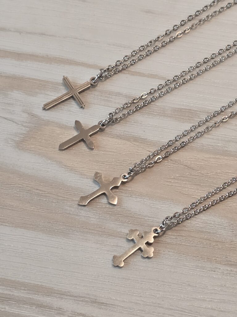 A lineup of stainless steel cross necklaces displayed on a light wooden surface. Each pendant features a unique design — from minimalist to ornate — showcasing craftsmanship and durability. Perfect for highlighting faith‑inspired jewelry and modern stainless steel accessories.