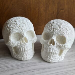 A pair of 3D‑printed sugar skulls in smooth white finish, featuring intricate floral and swirl engravings. The detailed craftsmanship highlights the Day of the Dead‑inspired design, perfect for collectors or festive décor.