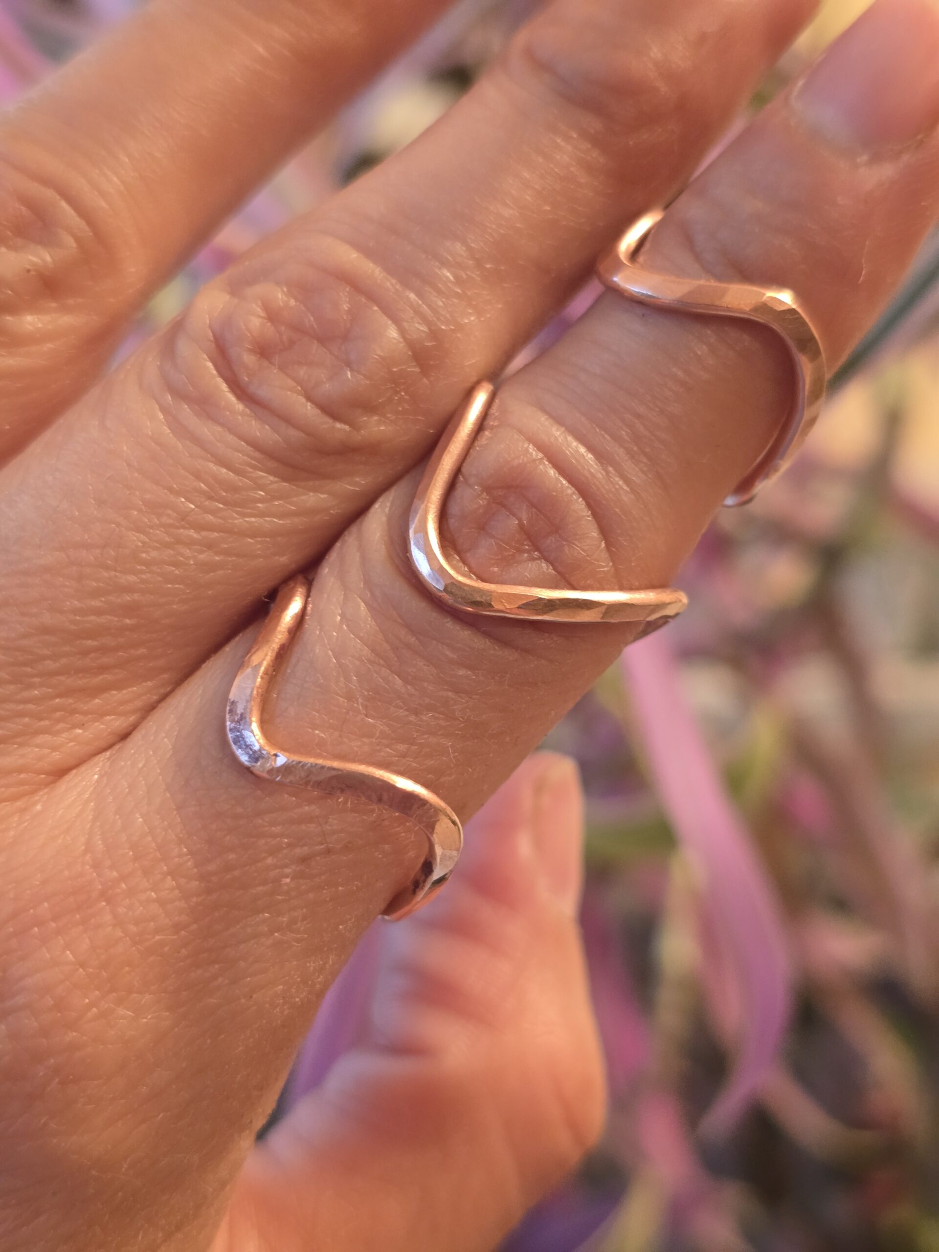 A close‑up of 3 handmade copper rings with a wavy, hammered design, worn elegantly on the fingers. The warm metallic tone and organic curves highlight the artisan craftsmanship and minimalist aesthetic.