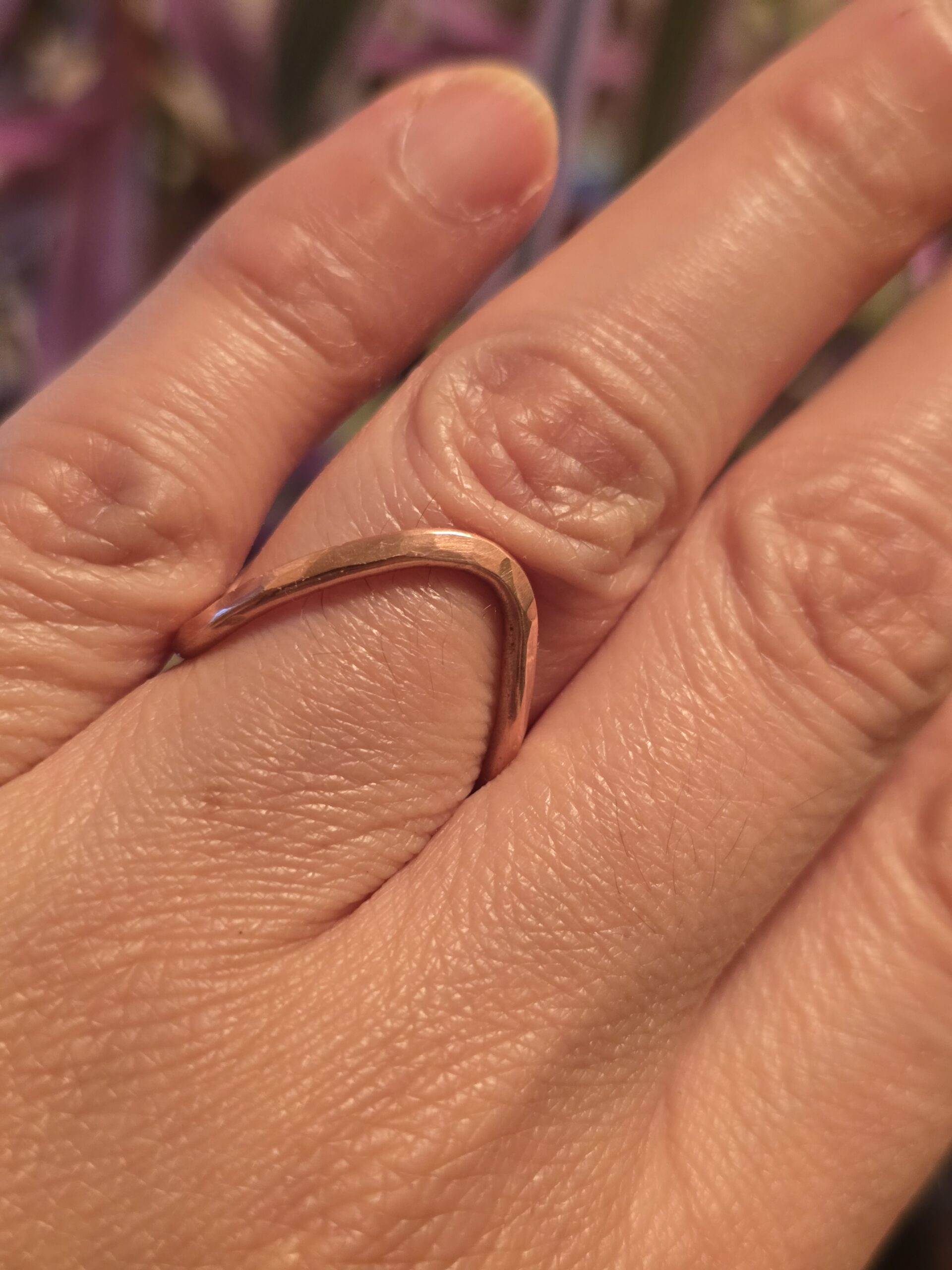 A detailed view of a hand‑forged copper ring showing its smooth curve and polished surface. The organic shape and warm tone evoke natural elegance and timeless simplicity.