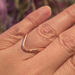 A handmade copper ring with a subtle V‑shaped curve, worn on the finger. The warm hue and hammered texture catch the light beautifully, perfect for everyday wear or stacking with other minimalist pieces.