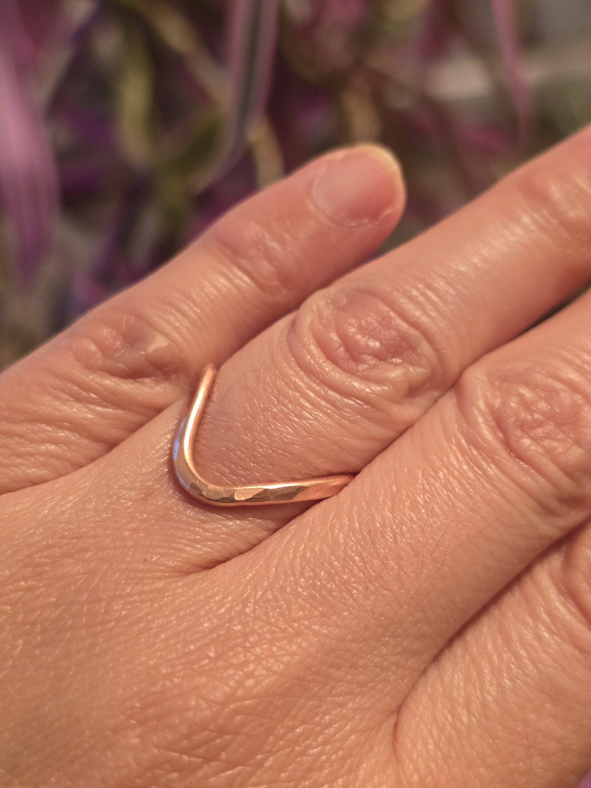 A handmade copper ring with a subtle V‑shaped curve, worn on the finger. The warm hue and hammered texture catch the light beautifully, perfect for everyday wear or stacking with other minimalist pieces.